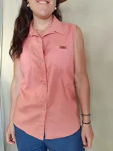 Musculosa tipo camisa con cuello camisero, cierre frontal de botones y dos bolsillos delanteros en el pecho. Diseño a rayas verticales en tonos celeste y blanco.