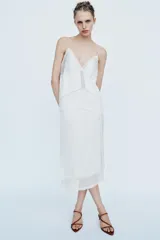 Falda midi de tiro medio, color blanco, confeccionada en hilatura de viscosa 100%, con detalle de aplicación de tejido combinado semitransparente con abertura en el bajo y cierre lateral con cremallera oculta.