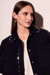 Sobrecamisa negra de algodón con corte oversize, cuello clásico, cierre frontal con botones a presión, dos bolsillos de parche en el pecho y apliques metálicos en cuello y solapa.