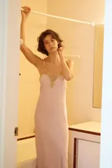 Vestido midi de satén en color rosado, con escote en pico y tirantes finos. Presenta detalles de encaje en color dorado a contraste en el escote y en el ruedo.