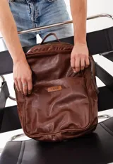 Mochila de cuero genuino color marrón, con diseño minimalista, compartimento principal con cierre, bolsillo frontal con etiqueta de marca y correas ajustables.