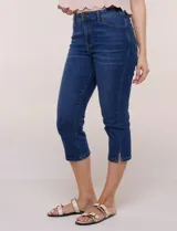 Pantalón capri de jean azul con calce ajustado, tiro alto, cinco bolsillos, cierre frontal con botón y pequeños tajos en los ruedos.