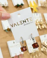 Aros tipo argolla de acero con dije colgante en forma de cubo de cristal color marrón.