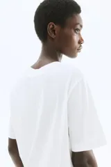 Remera de manga corta y cuello redondo, color blanco, con estampado frontal en negro que incluye la palabra "FLEURI", una ilustración abstracta de una hoja o flor y el texto "LA BEAUTÉ DE LA NATURE PARIS, 1978".