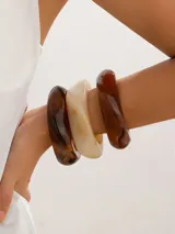 Set de tres brazaletes anchos y rígidos de resina, con acabado brillante. Los colores son ámbar translúcido, blanco hueso opaco y marrón oscuro translúcido.