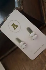 Par de aros tipo botón con dos piedras blancas ovaladas engarzadas en metal dorado.