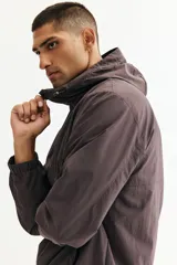 Campera rompevientos de nylon repelente al agua, color gris oscuro/marrón topo, con forro de malla. Presenta cierre frontal con protección para el mentón, capucha ajustable con cordón, bolsillos laterales y bolsillo interior con cierre, y elástico revestido en puños y bajo.