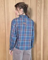 Camisa de manga larga con estampado de cuadros en tonos azules y rojizos. Presenta un cuello alto con volados y puños elásticos con detalle de volado en el extremo. Cierre frontal con botones ocultos.