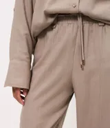 Pantalón carrot de viscolino color marrón, de corte amplio en la cadera y ajustado hacia los tobillos. Cuenta con cintura elástica en la parte posterior, lazo frontal para ajuste y caída liviana.