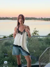 Blusa tipo lencera de satén color crema con escote en V y ruedo asimétrico, ambos decorados con encaje negro. Presenta breteles finos ajustables.