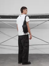 Riñonera negra de material impermeable (tracker waterproof) con tres bolsillos frontales con cierre y un bolsillo lateral. Incluye correa regulable con broche de mochila.