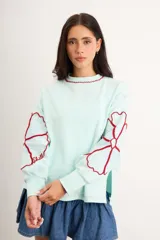 Buzo oversize de algodón con spandex, color verde menta, de manga larga con diseño de flores bordadas en rojo en las mangas y cuello redondo.