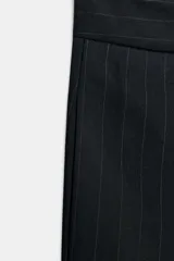 Pantalón de tiro medio color negro con raya diplomática, con pinzas delanteras, bolsillos laterales ocultos y pierna ancha. Cierre frontal con cremallera, botón y ganchos metálicos.