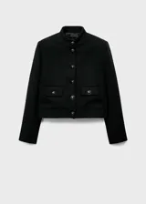 Chaqueta recta color negro con cuello mao, cierre frontal y bolsillos delanteros con solapa y botones joya.