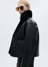 Chaqueta de doble faz con exterior de cuero sintético negro y forro interior de pelo sintético al tono. Presenta cuello camisero, cierre frontal con botones, manga larga y dos bolsillos de parche delanteros.