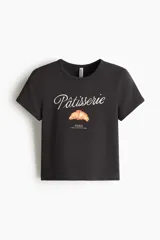 Remera corta de algodón color gris oscuro, con cuello redondo, mangas cortas y estampa frontal con la frase "Pâtisserie Paris" y un dibujo de un croissant.