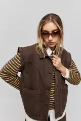 Chaleco de jean negro, de calce relajado con hombros caídos, cuello camisero, cierre frontal con botones y grandes bolsillos aplicados.