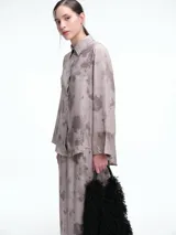 Camisa oversize de lyocell con estampado orgánico efecto lavado. Presenta cuello clásico, cierre frontal con botones, mangas amplias con puños anchos y un diseño de corte relajado con ruedo asimétrico, siendo más largo en la parte posterior.