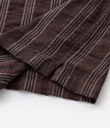 Camisa de manga corta con cuello solapa y cierre frontal de botones. Presenta un diseño de rayas verticales con textura jacquard en tonos marrones.