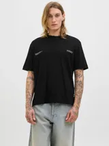 Remera negra de manga corta y cuello redondo, con un estampado gráfico en la espalda que muestra una escena urbana con edificios y texto que incluye "Metropolitan Scenes 1990" y el logo "JACK&JONES WORLDWIDE".