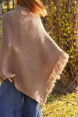 Poncho tejido en lana merino color marrón, con diseño de punto acanalado y terminación con flecos en el borde inferior. Incluye una pequeña etiqueta de cuero en la parte posterior.