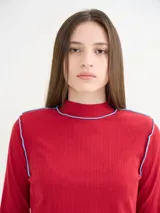 Polera de manga larga confeccionada en tela rib color bordó, con cuello alto y hombreras. Presenta costuras a la vista con pespuntes en hilo de color contrastante en el cuello, puños, hombros y ruedo.