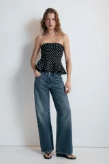 Top de escote recto y hombros descubiertos, color negro con estampado de lunares blancos. Presenta diseño entallado con bajo acabado en peplum y cierre lateral con cremallera oculta.
