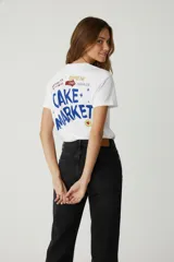 Remera de algodón de manga corta con cuello redondo y calce holgado. Presenta un estampado gráfico frontal con letras y una ilustración de cítricos en tonos naranja y marrón sobre fondo blanco.