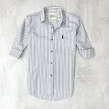 Camisa de manga larga a rayas verticales grises y blancas, con cuello clásico, cierre con botones y logo bordado en el pecho.