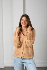 Cárdigan de punto color beige con textura calada de motivos florales, cuello alto, cierre frontal con botones y mangas largas con terminaciones acanaladas.
