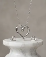 Set de joyería compuesto por collar con dije de corazón y aros tipo caravanas a juego, ambos con diseño minimalista de corazón abierto en acero.