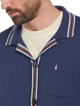 Cardigan azul marino de punto con cuello solapa, cierre abotonado, bolsillos delanteros y logo bordado en el pecho. Presenta ribetes a rayas en cuello, puños y bajo.