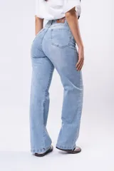 Jeans de mezclilla azul claro, tiro alto, corte wide leg y roturas a la altura de las rodillas.
