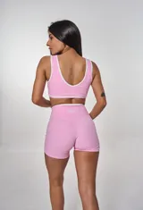 Conjunto deportivo compuesto por un top de escote redondo con ribetes blancos y un short de tiro alto con cintura cruzada en V. Ambas prendas son de color rosa liso.