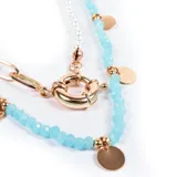 Collar corto de cuentas facetadas color celeste, con detalles dorados y dijes circulares. Incluye collar de perlas sintéticas y cadena de eslabones dorados con cierre marinero.