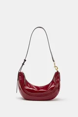Bolso de hombro de diseño semicircular, confeccionado en material sintético efecto charol de color rojo. Cuenta con una correa ajustable fina con detalles metálicos dorados y cierre superior con cremallera.