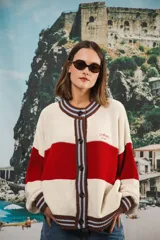 Cardigan oversized de punto grueso, color azul marino y blanco con franjas rojas y rosadas en el cuello, puños y solapa. Tiene botones grandes marrones y el logo de Anthea bordado en el pecho.