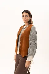 Chaleco oversize confeccionado en cuero descarne, con diseño de terminación en picos, detalle de tachas metálicas en los bordes frontales y flecos en la espalda.