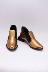 Zapato de cuero color dorado con elásticos laterales negros, taco cuadrado negro y tirador trasero.