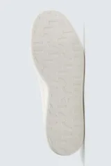 Zapatilla de cordones confeccionada en piel, con horma redonda y suela a tono. Presenta un diseño minimalista con detalle de contraste en el borde del talón.
