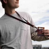 Llavero para el cuello con cinta de tela estampada a cuadros en tonos rosa, azul y naranja. Tiene un mosquetón metálico color bronce y un aplique de cuero sintético marrón con el logo de la marca.