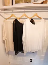 Blusa de seda blanca con corte holgado, cuello redondo y mangas cortas con caída suave. Presenta un diseño minimalista con espalda ajustable mediante lazo.