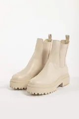 Bota tipo chelsea con suela track de goma en color marrón y capellada de cuero negro. Presenta elásticos laterales y tirador trasero.