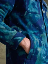 Sobrecamisa de tejido polar con estampado abstracto en tonos rojizos y azul marino. Presenta cuello clásico, cierre frontal con botones a presión, dos bolsillos frontales con solapa en el pecho y un parche decorativo.