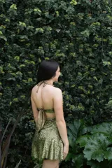 Vestido corto de lentejuelas color ciruela o morado oscuro, con escote corazón y detalle de argolla central que conecta con tirantes finos que atan al cuello. Presenta aberturas laterales (cut-outs) en la zona de la cintura y falda corta con vuelo.