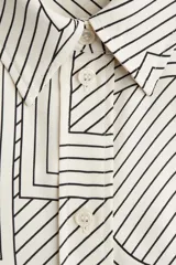 Camisa de manga larga con cuello camisero y cierre frontal de botones. Presenta un estampado geométrico en blanco roto y negro, compuesto por líneas rectas y curvas que forman patrones abstractos.