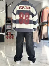 Buzo polo de rayas horizontales en gris oscuro y blanco, con cuello camisero, cierre frontal parcial y corte oversize. Presenta un gran número 88 estampado en la espalda en color bordó junto con la inscripción VCP/ARG.
