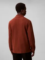 Chomba de manga larga Calvin Klein color marrón, con cuello clásico, cierre frontal con botones y logo bordado en el pecho.