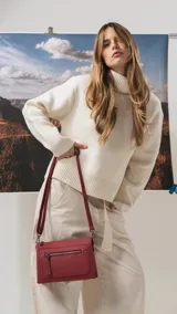 Bandolera de tamaño mediano en color gris, confeccionada en símil cuero con textura granulada. Presenta un bolsillo frontal con cierre, herrajes metálicos oscuros y correa ajustable y desmontable.