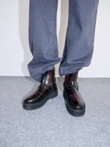 Bota corta de cuero negro tipo biker, con suela track de goma, plataforma, costuras y bordados decorativos en hilo rojo. Presenta tiras con hebillas metálicas y cierre en la parte trasera.